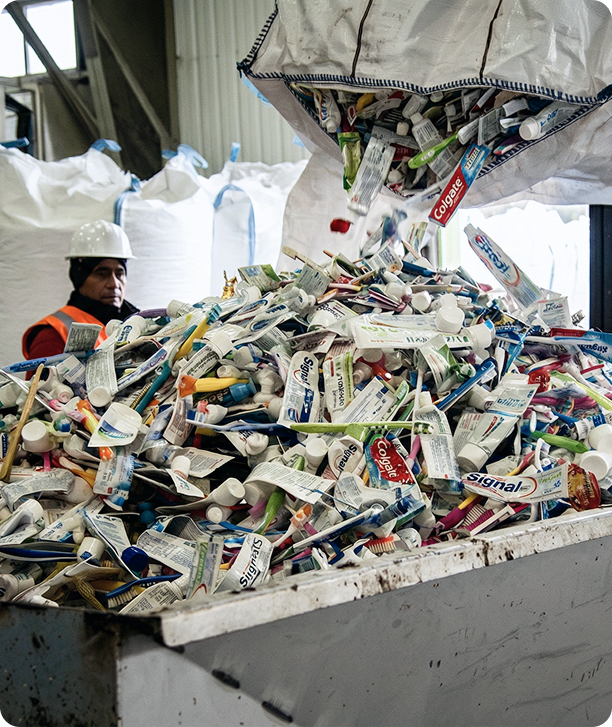 Worker in a recycling facility watches as a large bag empties used toothpaste tubes into a collection bin.